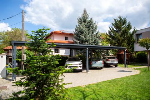 Napelemekkel fedett, extra hosszú, négy állásos kocsibeálló rétegragasztott fa szerkezettel.